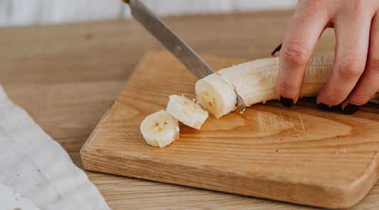 Hand schneidet Banane in Scheiben auf Holzbrett