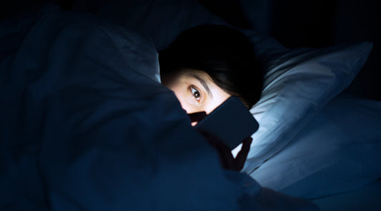 Frau liegt nachts im Bett und schaut aufs Handy