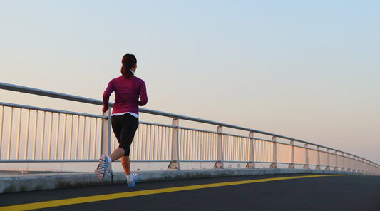 Frau joggt bei Sonnenaufgang auf einer Brücke