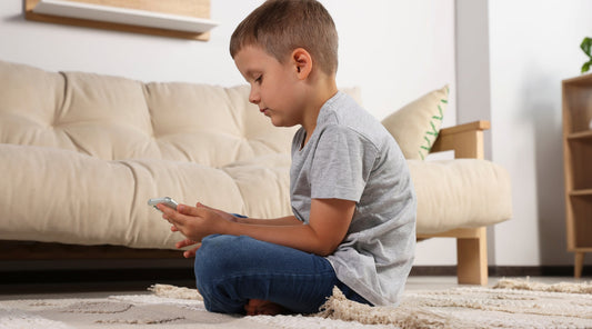 Alt Text: Junge mit schlechter Haltung beim Sitzen am Boden nutzt Smartphone im Wohnzimmer.