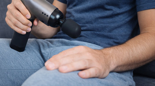Mann Massagepistole in der Hand auf der Couch