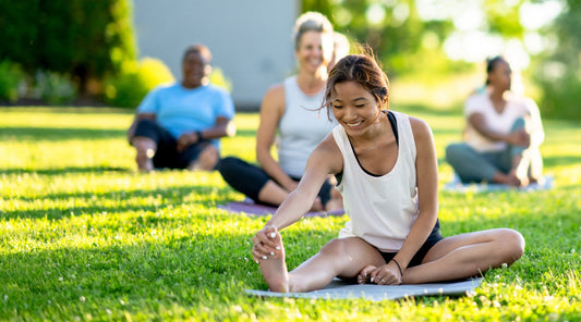 Frau macht Dehnübung im Park auf Yogamatte