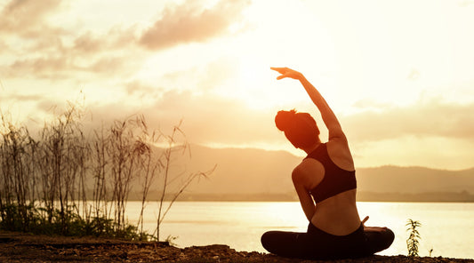 Frau macht Yoga-Übung im Sonnenuntergang am Wasser