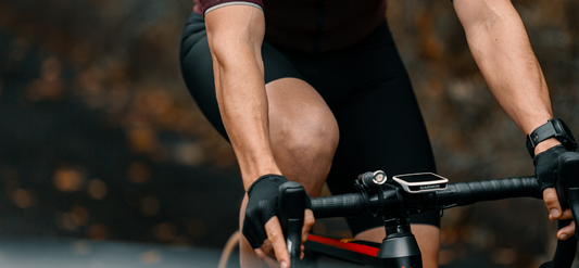 Nahaufnahme eines Radfahrers in Sportkleidung auf einem Rennrad. Er trägt Handschuhe, eine Sportuhr und nutzt einen Fahrradcomputer. Der Hintergrund ist unscharf mit herbstlichen Farben.
