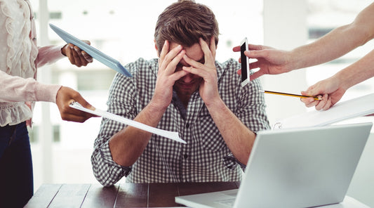 Gestresster Mann im Büro mit Laptop und vielen Aufgaben gleichzeitig