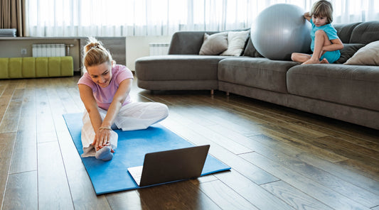 Frau macht Online-Workout zu Hause mit Kind im Hintergrund