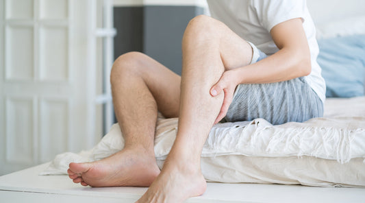 Mann hält sich mit Schmerzen die Wade im Schlafzimmer