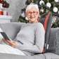 Ältere Frau entspannt mit OrthoMechanik Rücken-Massagegerät vor einem Weihnachtsbaum.