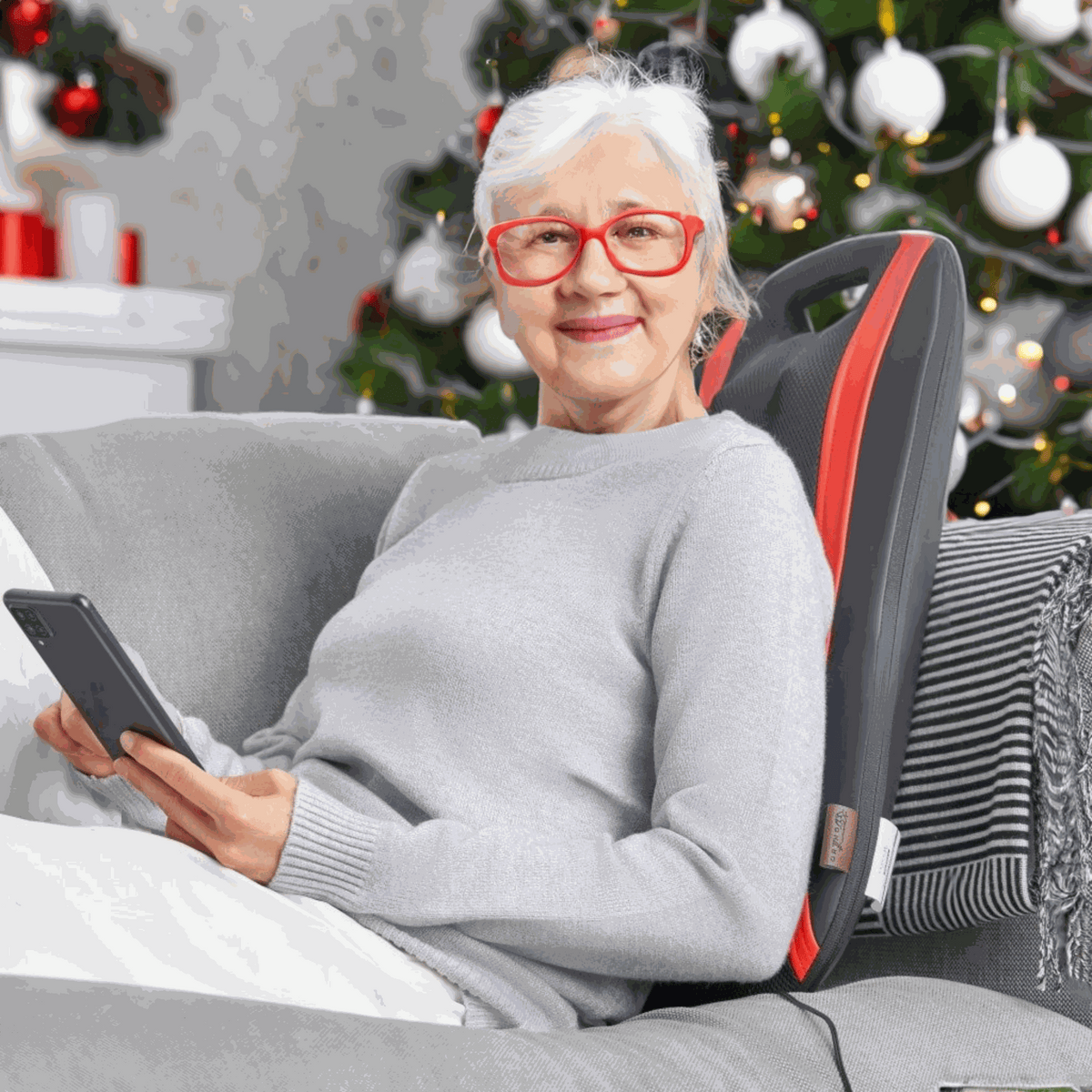 Ältere Frau entspannt mit OrthoMechanik Rücken-Massagegerät vor einem Weihnachtsbaum.